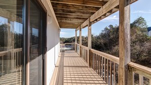 Une terrasse en bois avec une rambarde, de grandes fenêtres et une vue sur le paysage environnant.