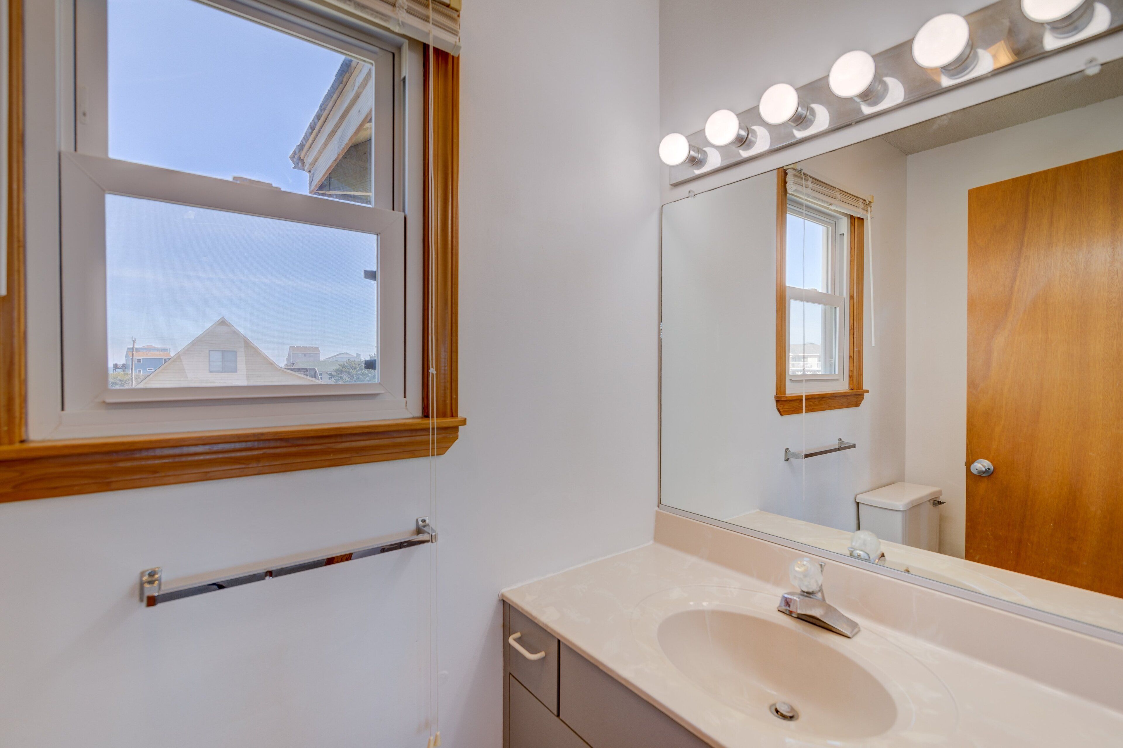 A bathroom with a large mirror, vanity, and a window with blinds.