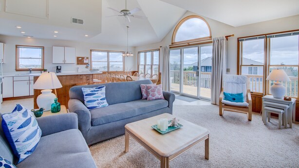 A spacious living room with a grey sofa, a wooden coffee table, and a view of the outdoors through large windows. - 2850 - SunDancer, Pet-Friendly Duck Retreat Near Beach & Town (Duck)