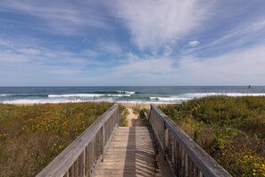 A wooden boardwalk leading to a beach with waves and a clear sky.