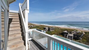 Eine Holztreppe führt zu einem Balkon mit Blick auf einen Strand und ein Schwimmbad.