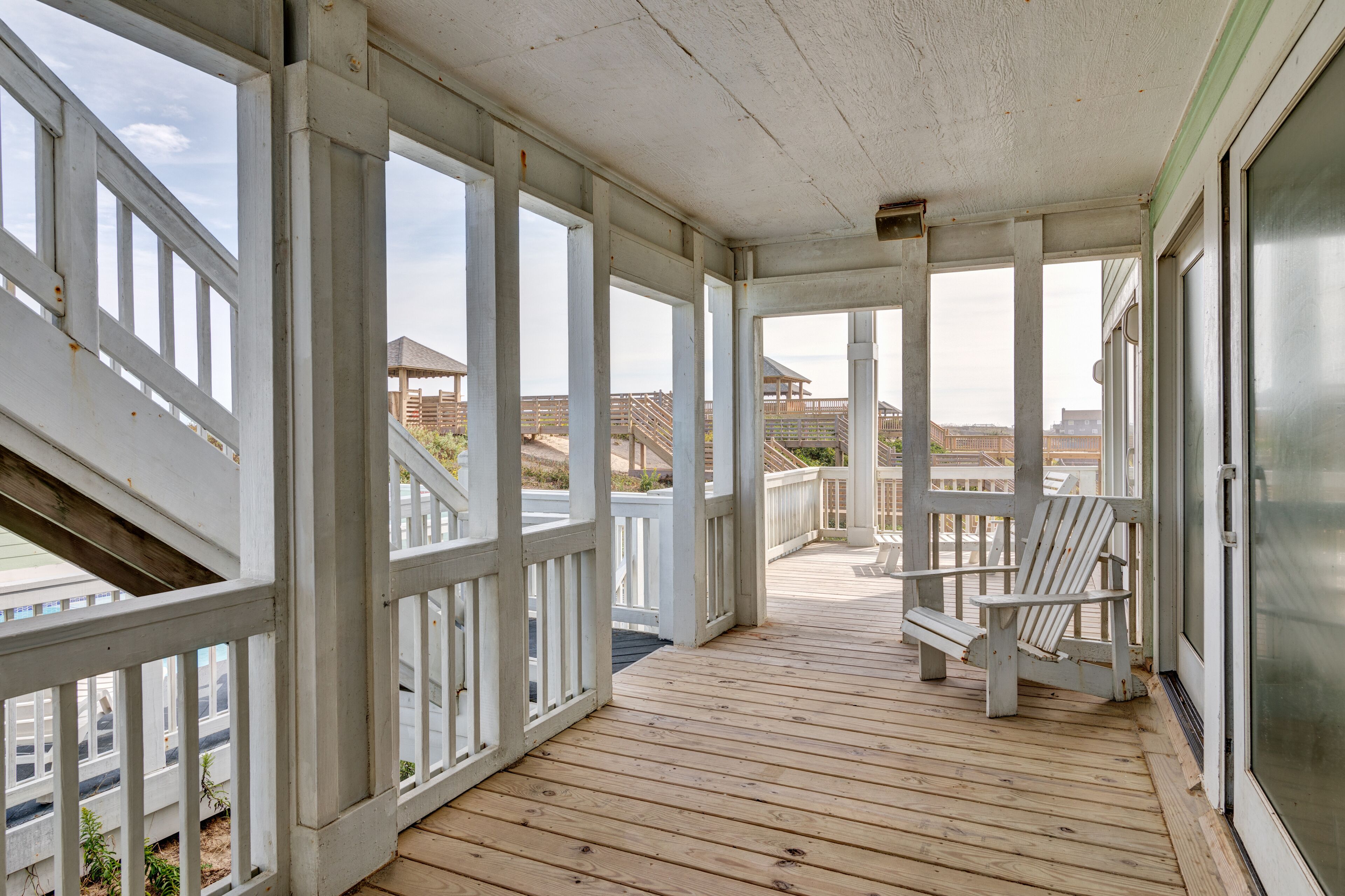 Una terraza cubierta de madera con barandillas blancas y una única silla Adirondack.
