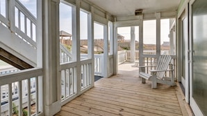 Eine überdachte Holzterrasse mit weißen Geländern und einem einzelnen Adirondack-Sessel.