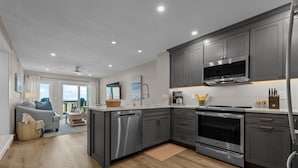 A modern kitchen with grey cabinets, stainless steel appliances, and a large window. - 5619- Pura Vida, Oceanfront fully equiped condo! (Nags Head)