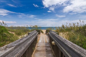 A wooden boardwalk leading to a beach with sand and grass on either side. - 5619- Pura Vida, Oceanfront fully equiped condo! (Nags Head)