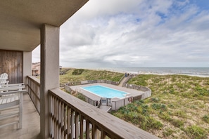 Una terraza de madera con piscina, con vista a una playa y al océano.