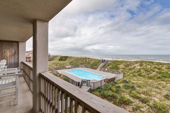Una terraza de madera con piscina, con vista a una playa y al océano.