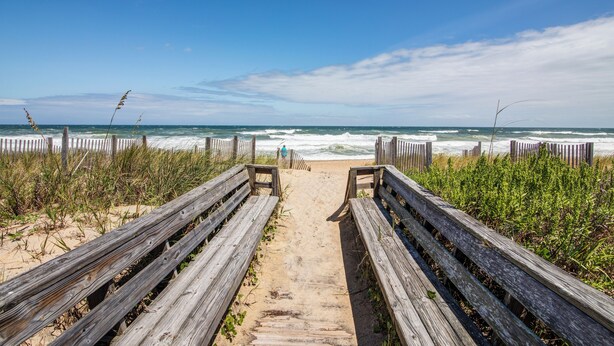 Un paseo marítimo de madera que conduce a la playa, con una persona a lo lejos.