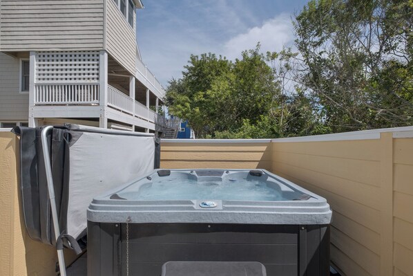 Un bain à remous équipé d’une pompe et d’un tuyau, une terrasse en bois et, au fond, un bâtiment doté d’un balcon.