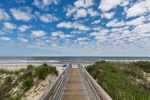 A wooden boardwalk leading to a beach with a clear sky and a few clouds.