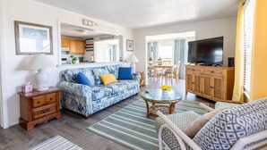 A living room with a blue patterned sofa, a wooden cabinet with a TV, and a dining area with a table and chairs. - 7847- Summerset - Dog Friendly Oceanfront Retreat in Frisco (Frisco)