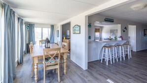 A spacious kitchen with wooden countertops and bar stools, a dining area with a wooden table and chairs, and a view of the outdoors through large windows. - 7847- Summerset - Dog Friendly Oceanfront Retreat in Frisco (Frisco)