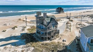 Une maison située en bord de mer, dotée d’un grand balcon, d’une tour et d’un bâtiment séparé à l’arrière-plan.