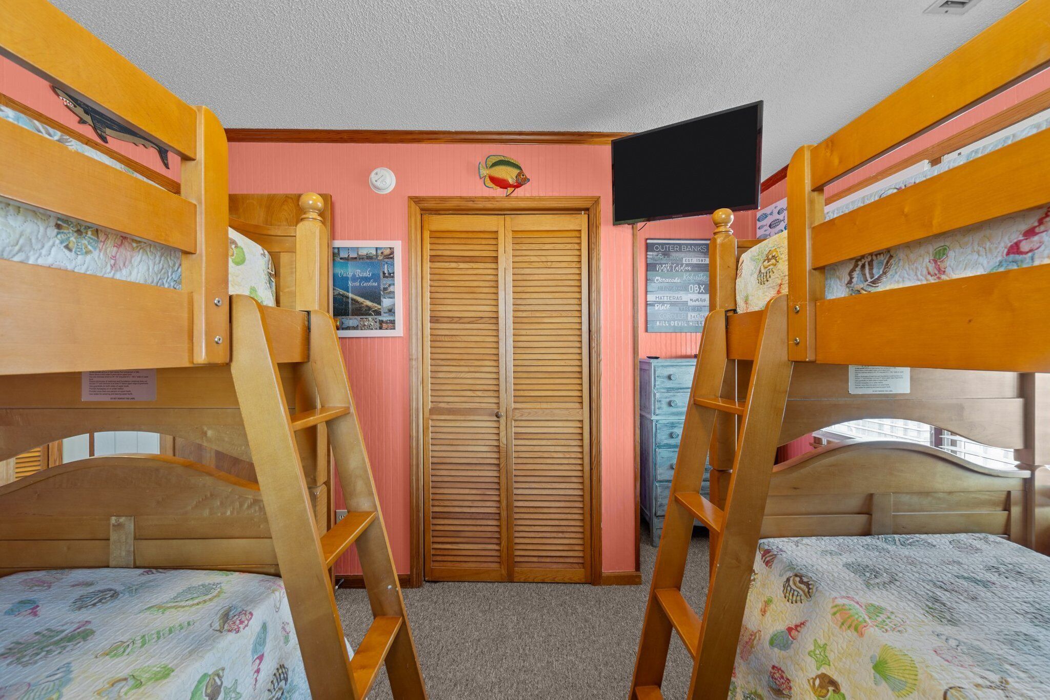 A bunk bed room with a wooden ladder, a closet with a sliding door, and a wall-mounted TV.