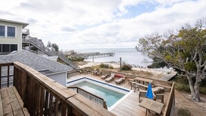Una terraza de madera con piscina, con vistas a una playa y un muelle.