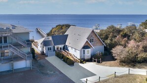 Una propiedad costera con una casa amplia que cuenta con un balcón destacado, un muelle que se adentra en el mar y vistas despejadas al océano.
