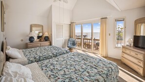 Un dormitorio con dos camas, ventilador de techo, cómoda, televisor y balcón con vista al mar.
