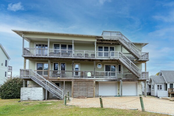 A multi-story building with balconies, a garage, and a gravel driveway. - 2817 - Aerescape, Soundfront Duck | Hot Tub, Elevator & Sunsets (Duck)