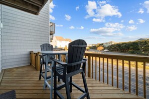Un terrazzo in legno con un tavolo e due poltrone Adirondack, con vista su una strada e delle case.
