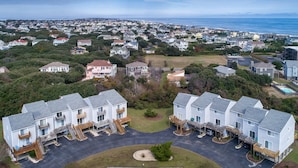 Uma área residencial com fileira de casas geminadas, com varandas, um estacionamento e vista para o mar.