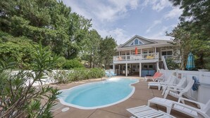 Une maison à deux étages avec une piscine, un espace salon extérieur et un balcon couvert.