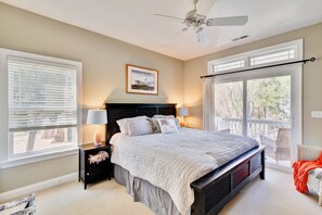 Une chambre à coucher avec un grand lit, un ventilateur de plafond, une table de chevet avec une lampe et une fenêtre avec des stores.