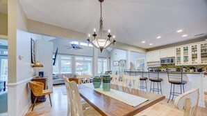 Un vaste espace dédié à la salle à manger, avec une table en bois, des chaises blanches et un lustre.