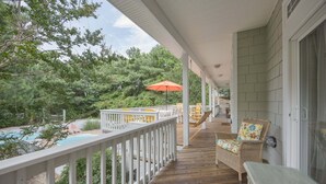 Une véranda couverte avec une terrasse en bois, des rampes blanches, du mobilier d’extérieur et une vue sur une piscine.