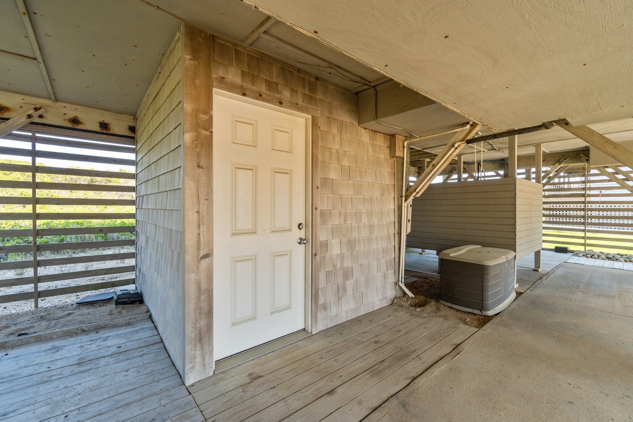 A covered porch with a wooden door, a concrete floor, and a small heater.