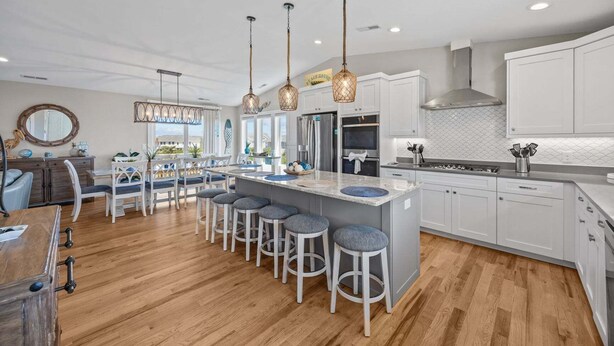 A modern kitchen with white cabinetry, a central island with bar stools, pendant lighting, and a view of the outdoors. - 3943 - Let it Beach - Walk to Duck Shops + Beach | Pool & Hot Tub (Duck)