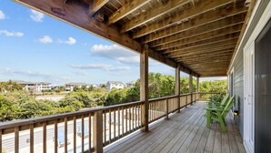 A wooden deck with a railing, green chairs, and a view of houses and greenery. - 3943 - Let it Beach - Walk to Duck Shops + Beach | Pool & Hot Tub (Duck)