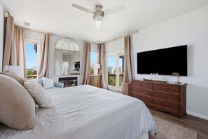 Un dormitorio con una cama grande, un aparador, un televisor y un balcón con cortinas.
