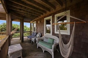 A covered porch with wicker furniture, including a sofa and chairs, and a hammock.