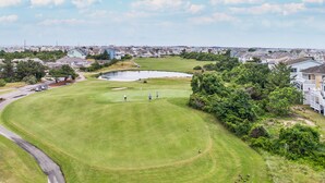 Ein Golfplatz mit Teich, Häusern im Hintergrund und einer sich schlängelnden Straße.