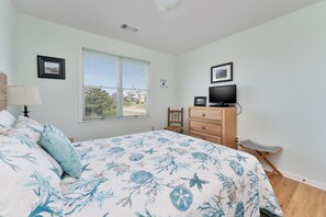 A bedroom with a bed, a dresser, a television, and a window with blinds.