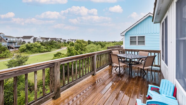 Eine Holzdielen-Terrasse mit Tisch und Stühlen, mit Blick auf eine grüne Landschaft und angrenzende Häuser.