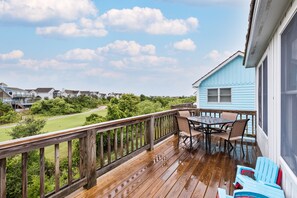 A wooden deck with a table and chairs, overlooking a green landscape and neighboring houses.
