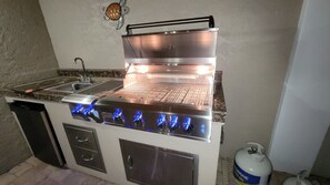 A stainless steel outdoor kitchen with a grill, a sink, and a propane tank.