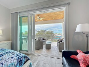 A hotel room with a bed, a balcony with wicker furniture, and a view of the cityscape.