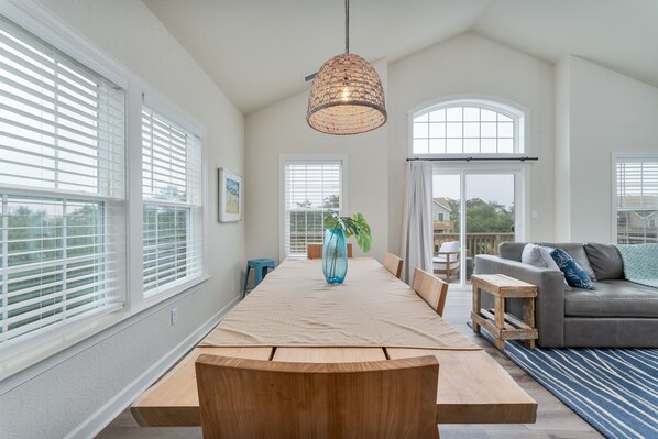 Relax in this stylish room with a long dining table, comfortable sofa, and a hanging light fixture.