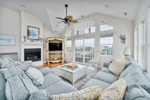 A spacious living room with a large gray sofa, a fireplace, and a ceiling fan.