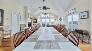 A spacious dining area with a long table, wooden chairs, and a ceiling fan. - 4763- Smells Like Sea Spirit, Kitty Hawk Beach House | Pool & Game Room (Kitty Hawk)