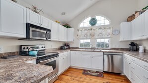 A kitchen with white cabinets, granite countertops, a stainless steel dishwasher, and a large window with a view. - 4763- Smells Like Sea Spirit, Kitty Hawk Beach House | Pool & Game Room (Kitty Hawk)