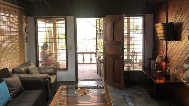 A cozy living room with a sofa, a glass coffee table, and a wooden door leading to an outdoor area. - Villa by the Sea (Playa Grande)
