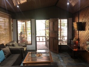A cozy living room with a sofa, a glass coffee table, and a wooden door leading to an outdoor area. - Villa by the Sea (Playa Grande)