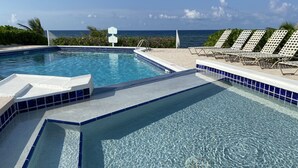 Une piscine d’un bleu éclatant, avec vue sur l’océan, entourée de chaises longues et d’une terrasse carrelée.