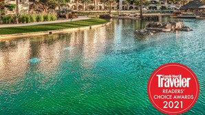 Un resort con varias edificaciones, una piscina central y palmeras.