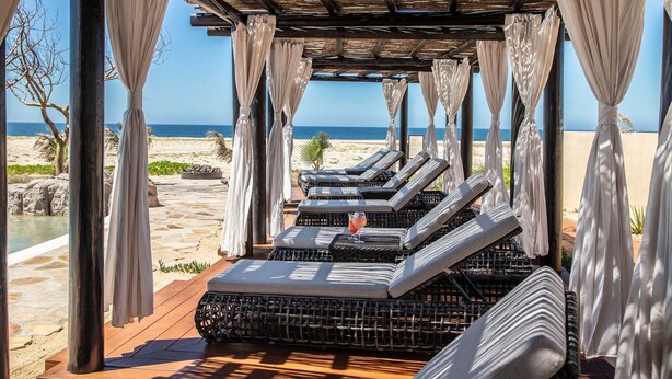 Un área de descanso frente a la playa con sillones acolchados, una terraza de madera y vista al océano.
