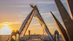 Un campamento en el desierto con una estructura grande similar a un tipi, decorada con plantas y luces, rodeado de faroles y una mesa con objetos encima.
