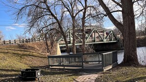 A paved walkway leading to a bridge over a body of water, with a metal railing and a tree on the right. - Newly remodeled Riverfront 3 bedroom house on the Great Chazy River with dockage (Champlain)